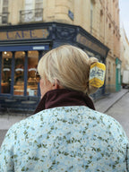 Person with a floral-patterned jacket and yellow butter claw clip walking past a cafe.
