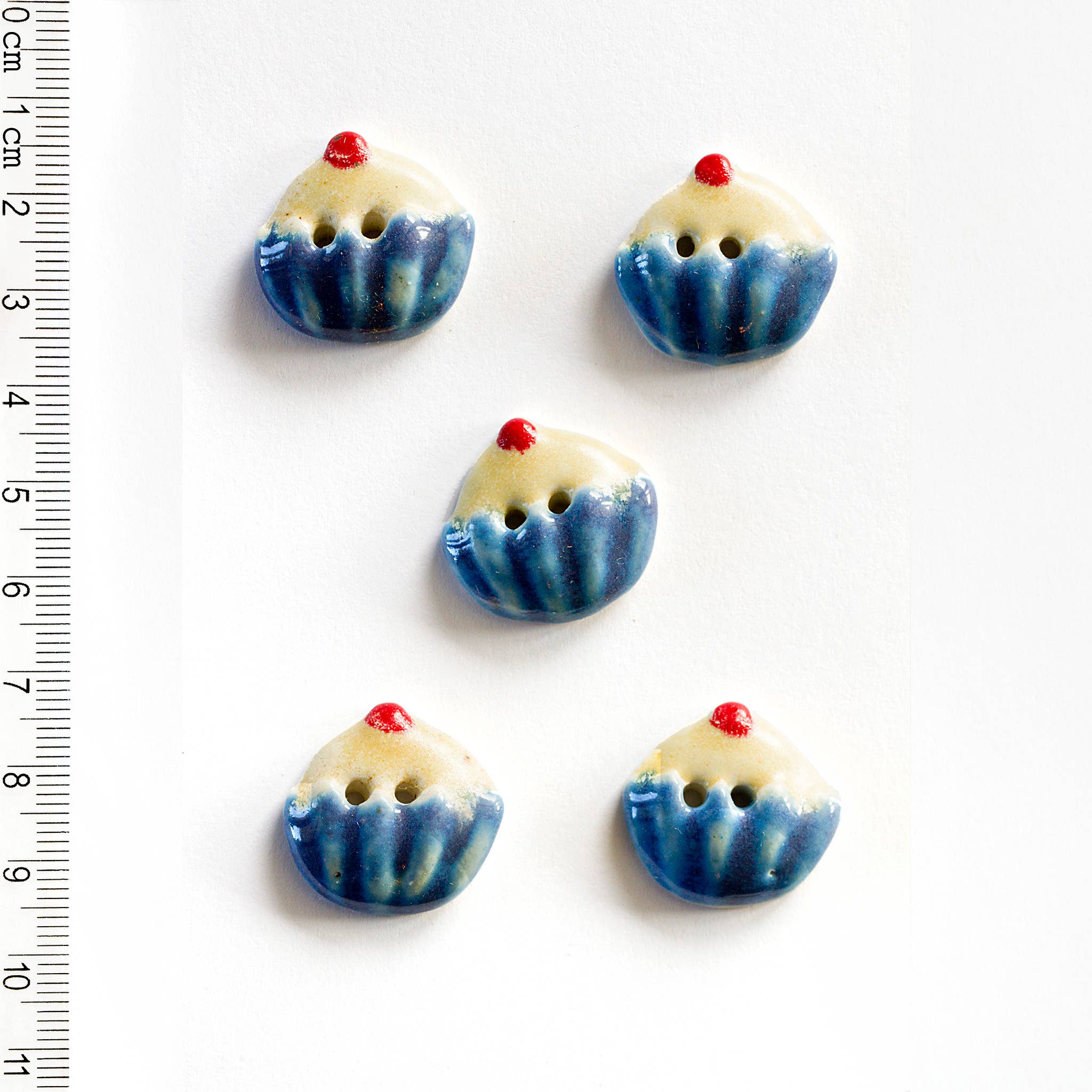 Five blue and white ceramic buttons shaped like small cakes on a white background with a ruler for scale.