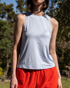 Person wearing a light gray sleeveless top and red shorts outdoors with trees in the background