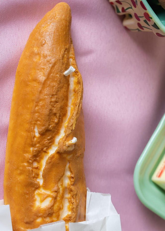 Candle shaped like a loaf of bread on a pink tablecloth. 