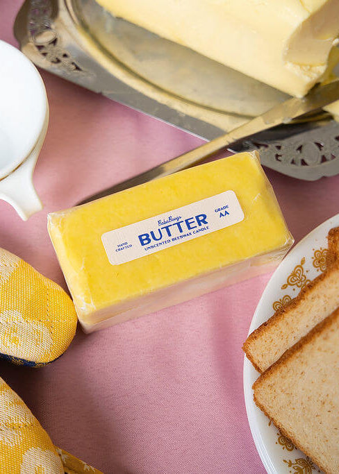 Butter candle, bread slices, and a measuring cup on a pink table cloth at breakfast.
