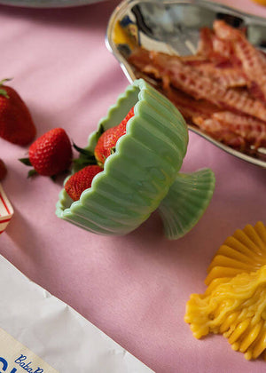 Green jadeite ceramic bowl with strawberries, pink tablecloth with breakfast food items and yellow candle.