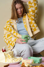 A person sitting with a green jadeite Inner Grandma mug, surrounded by breakfast foods and butter on a table.