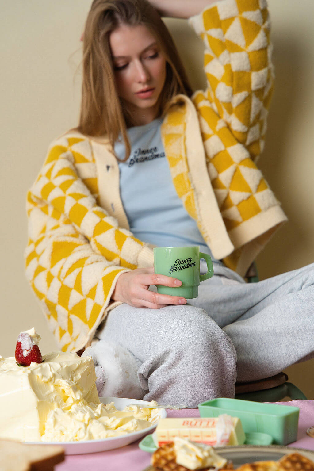 A person sitting with a green jadeite Inner Grandma mug, surrounded by breakfast foods and butter on a table.