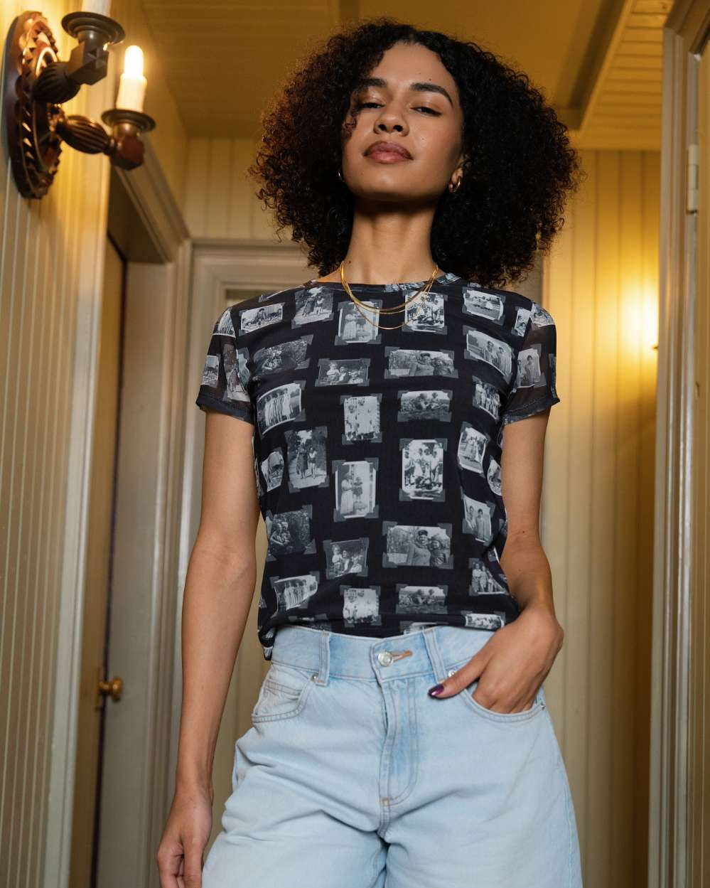 Front of person wearing black and gray mesh printed fabric top of black and white images of grandmas, people and objects with denim shorts standing indoors.