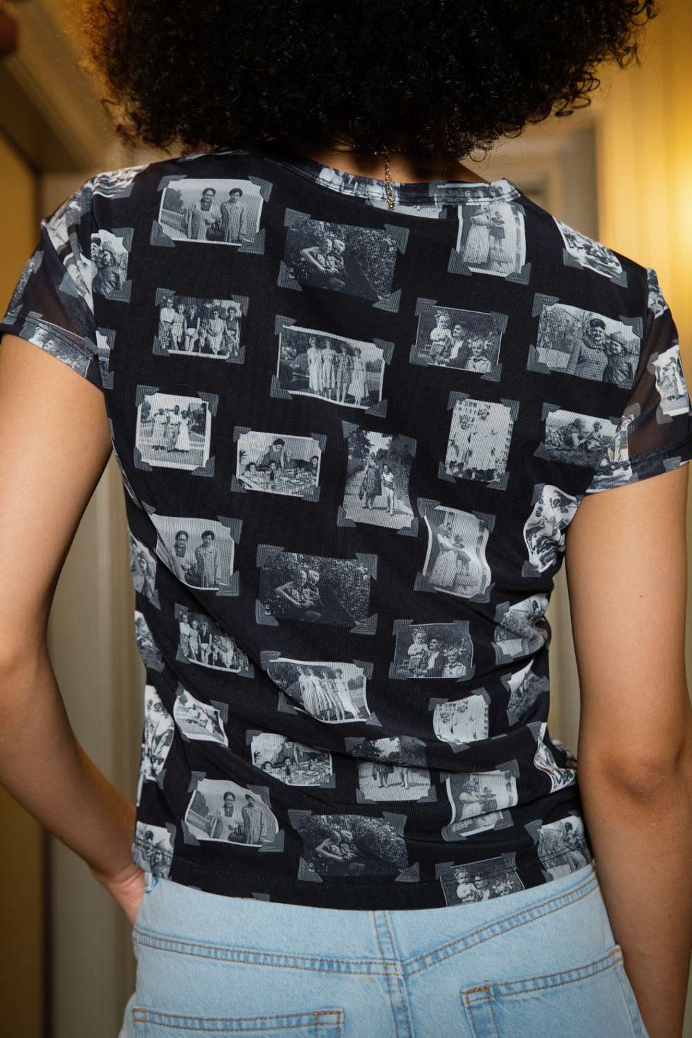 Back of person wearing black and gray mesh printed fabric top of black and white images of grandmas, people and objects with denim shorts standing indoors.