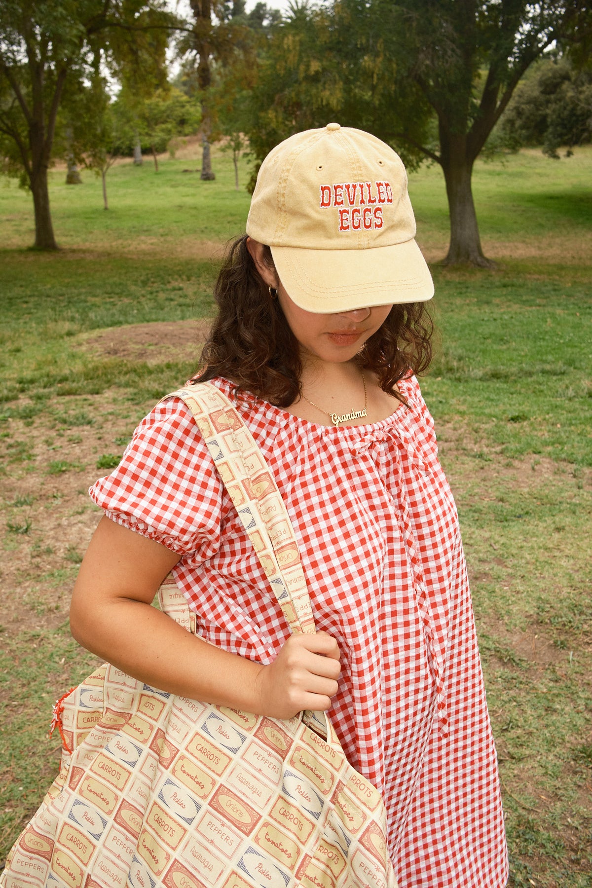 Person wearing a yellow hat with red "Deviled Eggs" lettering, a red-and-white dress, and holding a tote bag.
