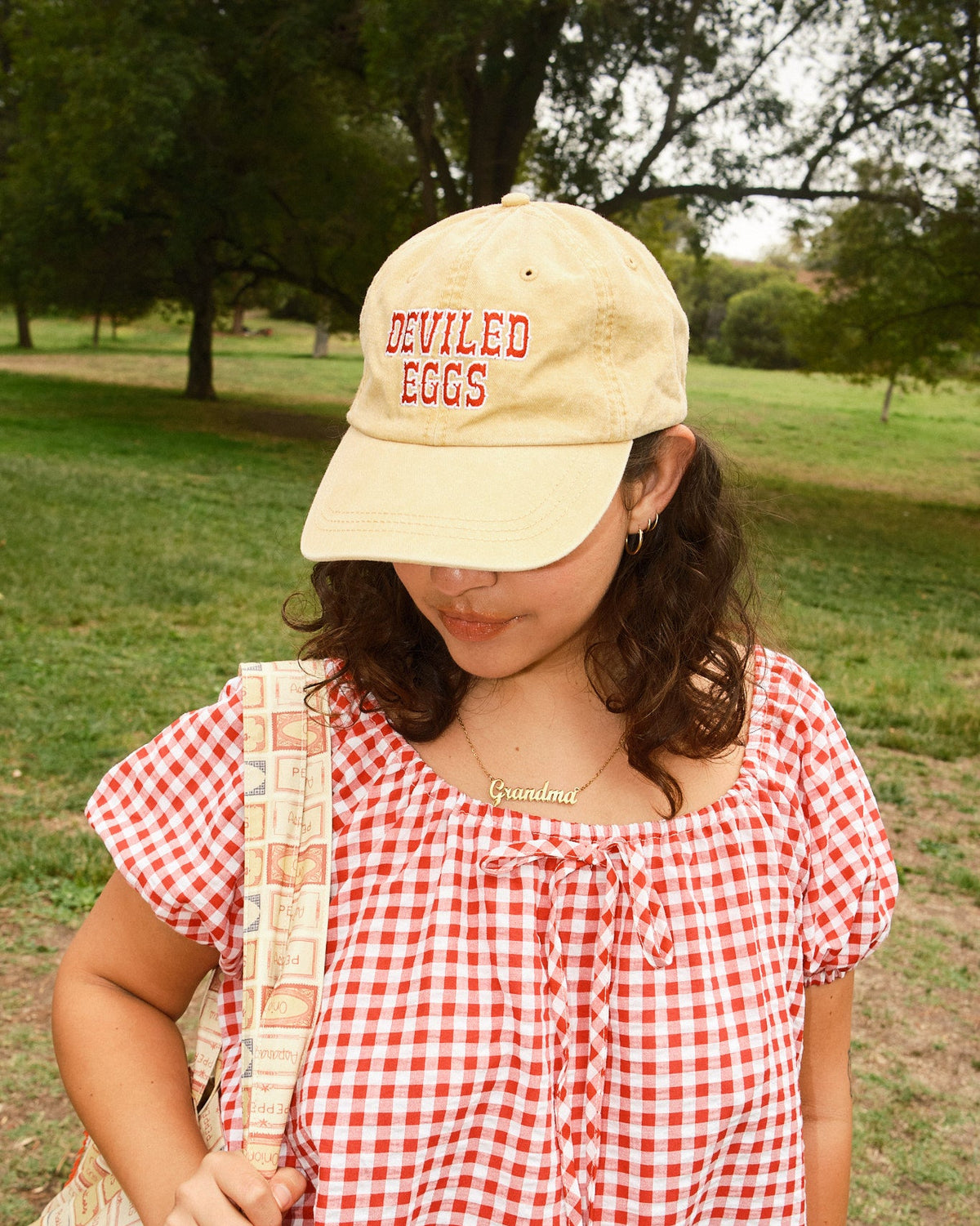 Person wearing a yellow hat with red "Deviled Eggs" lettering, a red-and-white dress, and holding a tote bag.