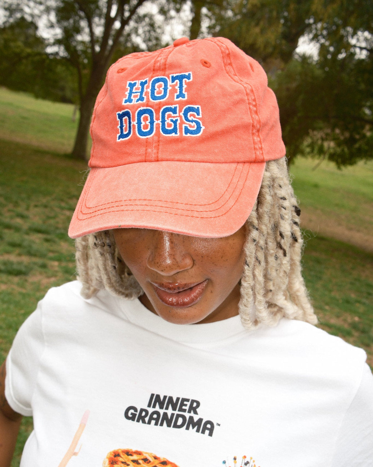 Person wearing a red baseball cap with blue "Hot Dogs" lettering and a white ringer T-shirt.