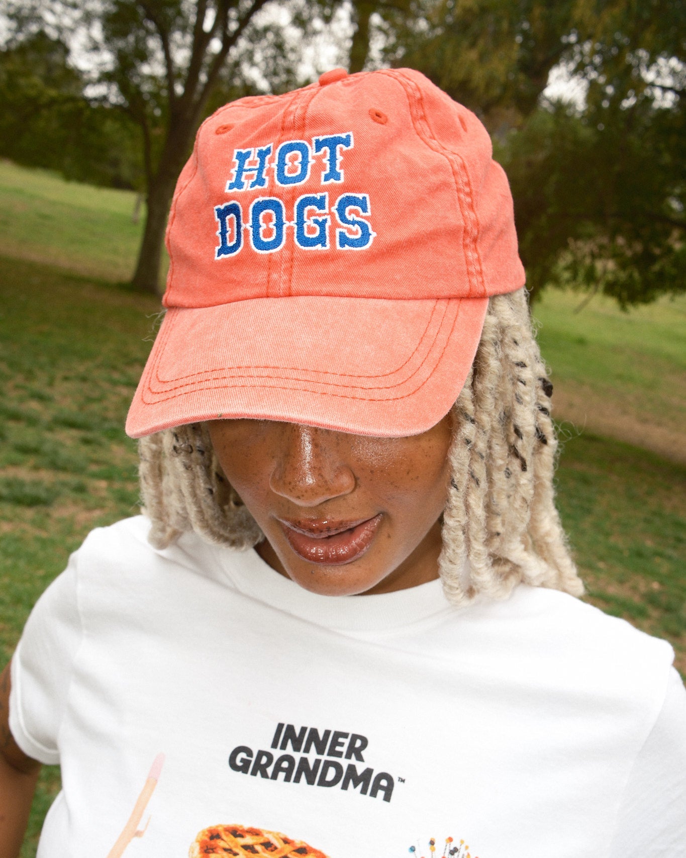 Person wearing a red baseball cap with blue "Hot Dogs" lettering and a white ringer T-shirt.