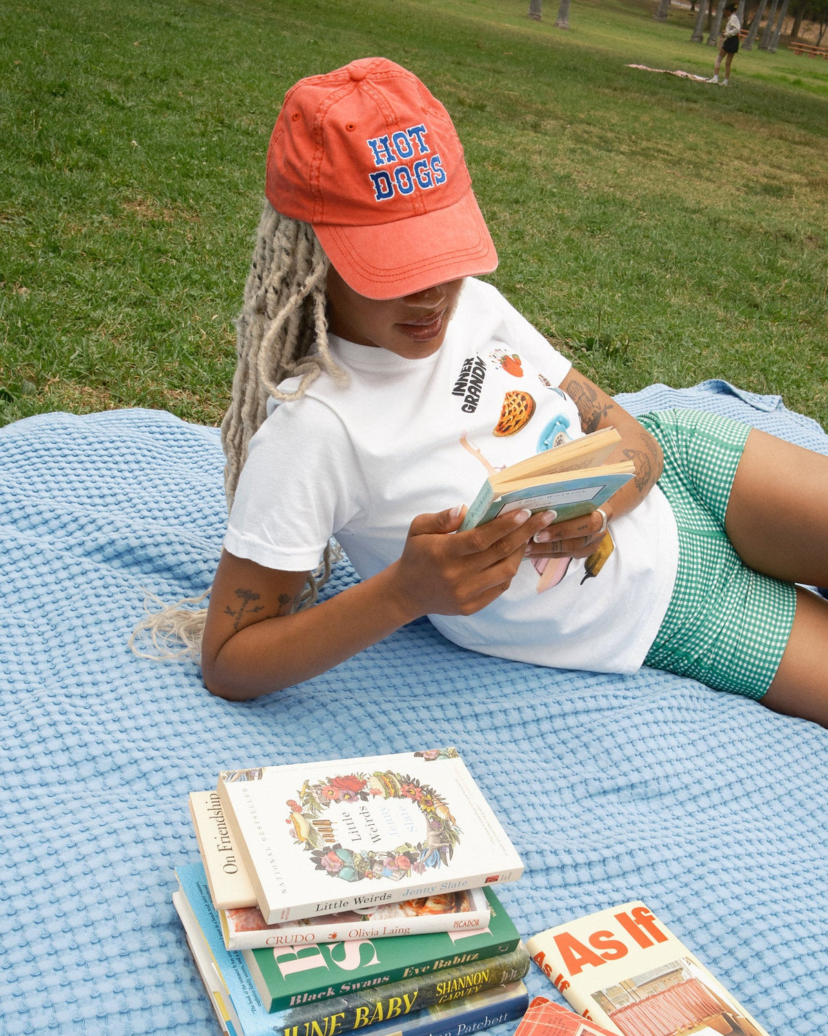 Person wearing a red baseball cap with blue "Hot Dogs" lettering and a white T-shirt and green biker shorts.