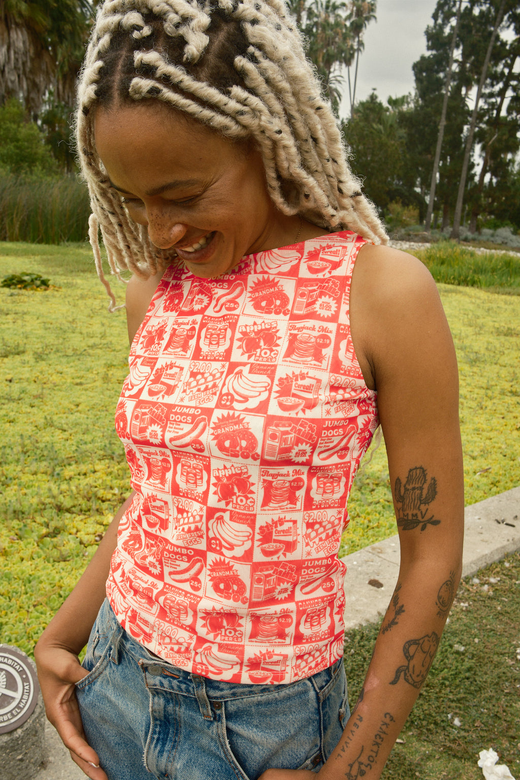 Person wearing a tank top with orange vintage-style food coupon pattern and jeans.