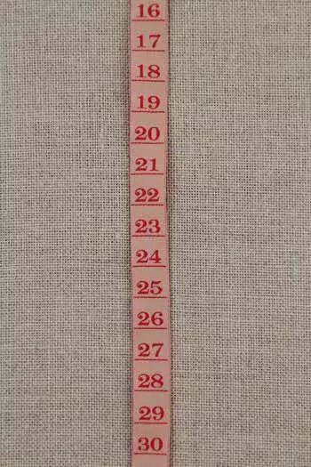 Measuring tape ribbon with red numbers on a textured beige background