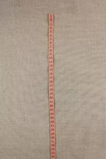 Measuring tape ribbon with red markings on a beige fabric background