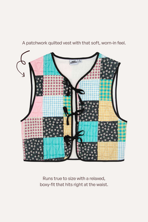 A patchwork quilted vest with a colorful grid of floral, gingham, and striped squares in pink, blue, yellow, black, and white. It features a V-neck, black trim, and three black cord ties at the front.