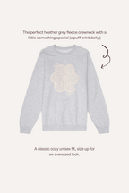 A light heather grey crewneck sweatshirt with a cream puff-print dolly graphic on the chest, shown on a light beige background with descriptive text and a brown arrow.