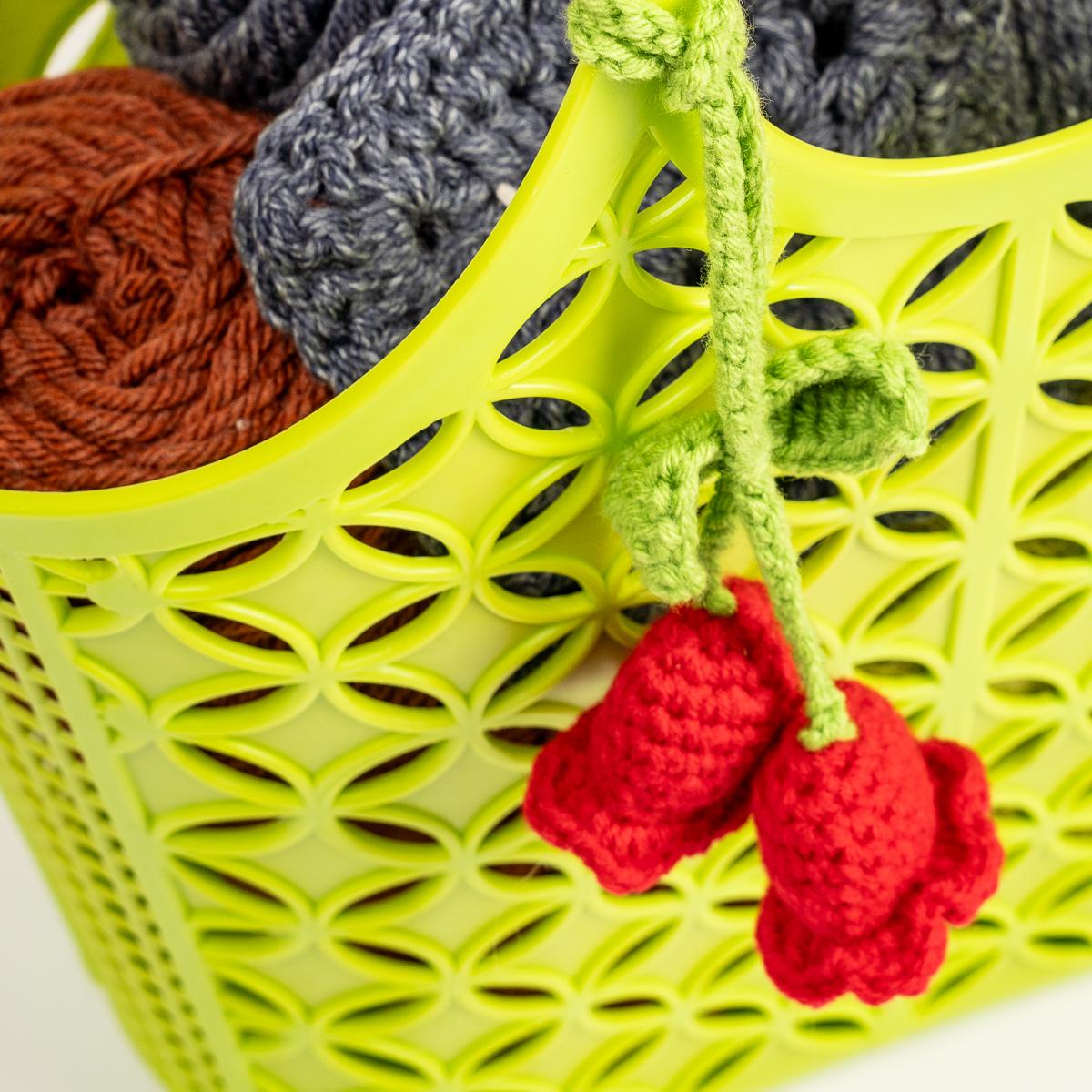 Green basket with yarn and a small knitted red flower on a white background