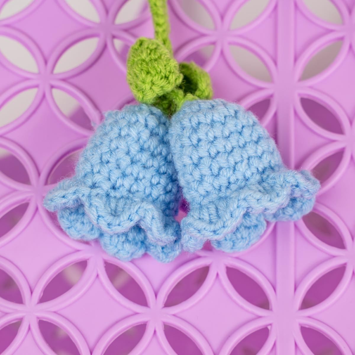 Crocheted blue flower with green stem on a pink patterned background