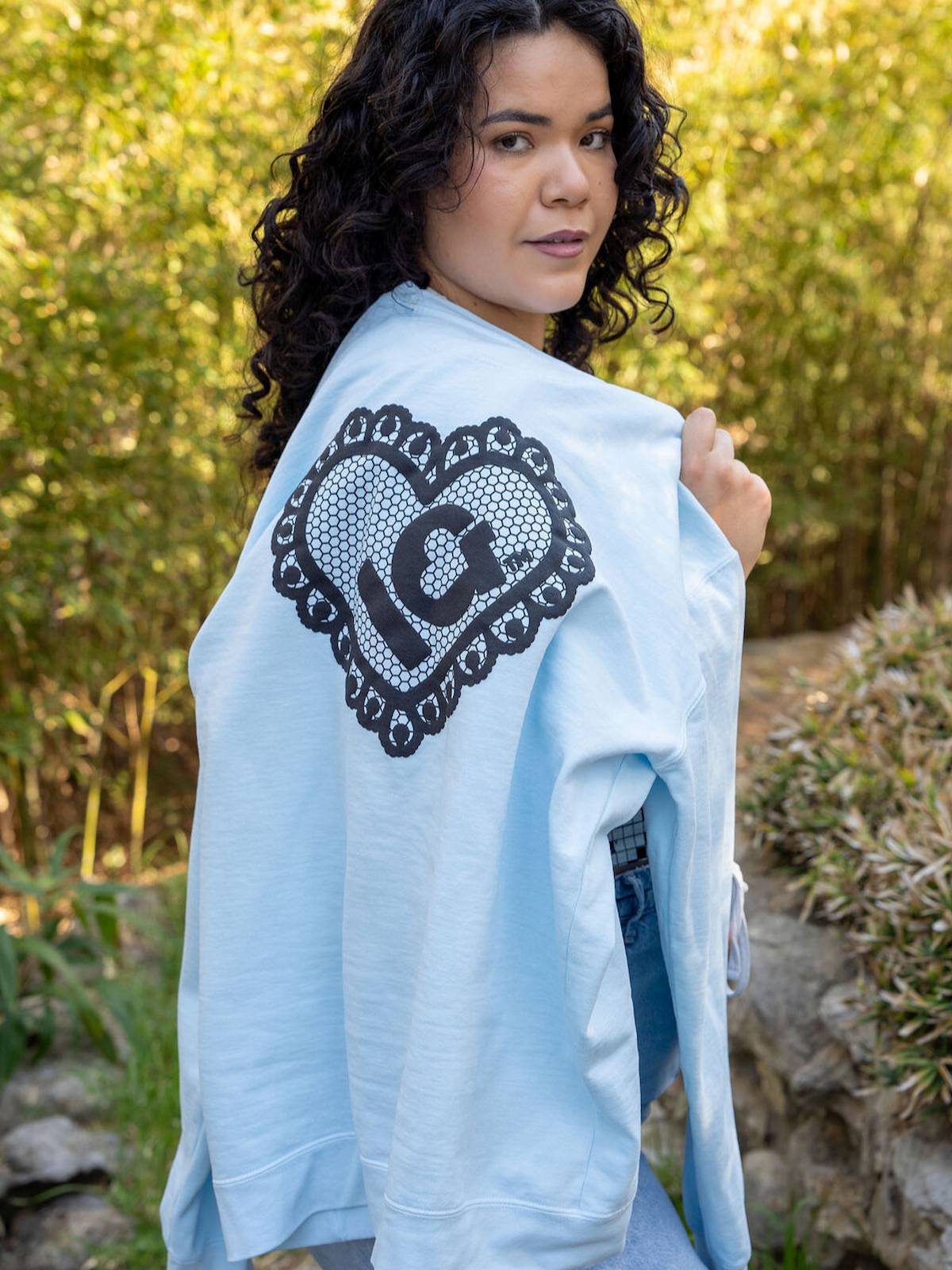 Woman holding a light blue jacket with a black heart design outdoors.