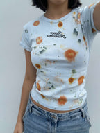 Person wearing a light blue cropped t-shirt with orange and yellow pattern naturally dyed by flowers with "Inner Grandma" text