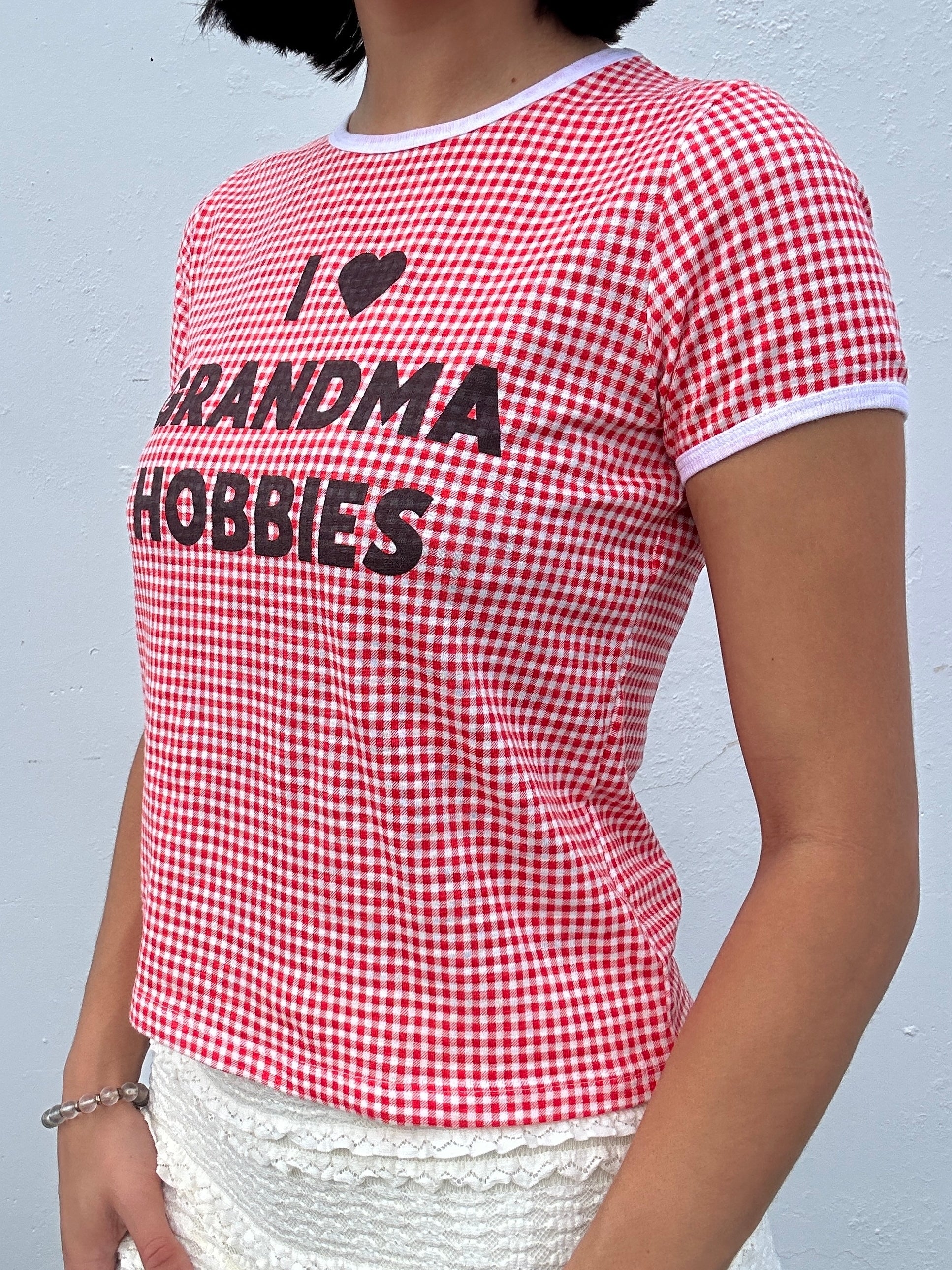 Red and white checkered "I Heart Grandma Hobbies" t-shirt with text worn by a person against a gray background