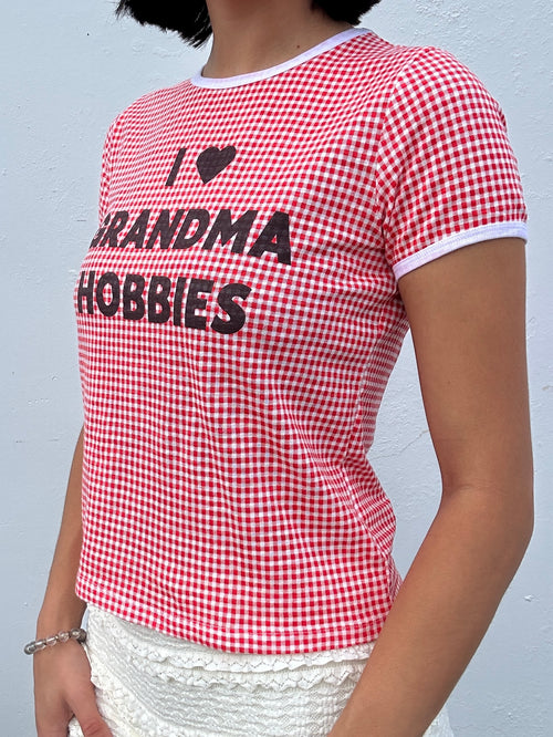 Red and white checkered "I Heart Grandma Hobbies" t-shirt with text worn by a person against a gray background