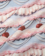 Close-up of fabric with wavy pink and purple frosting print and red cherries