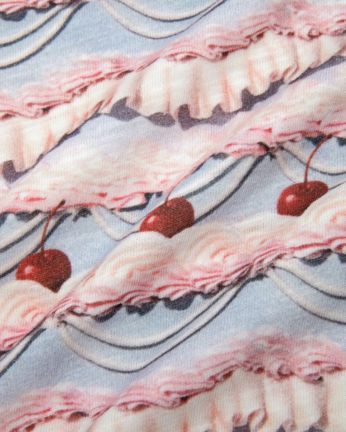 Close-up of fabric with wavy pink and purple frosting print and red cherries