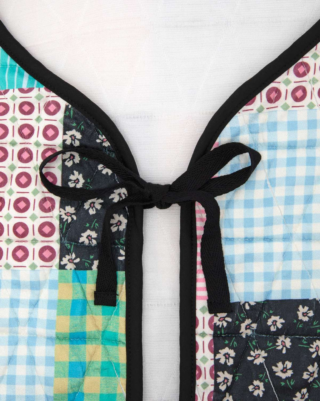 Up close of colorful patterned vest with a bow detail on a white background.