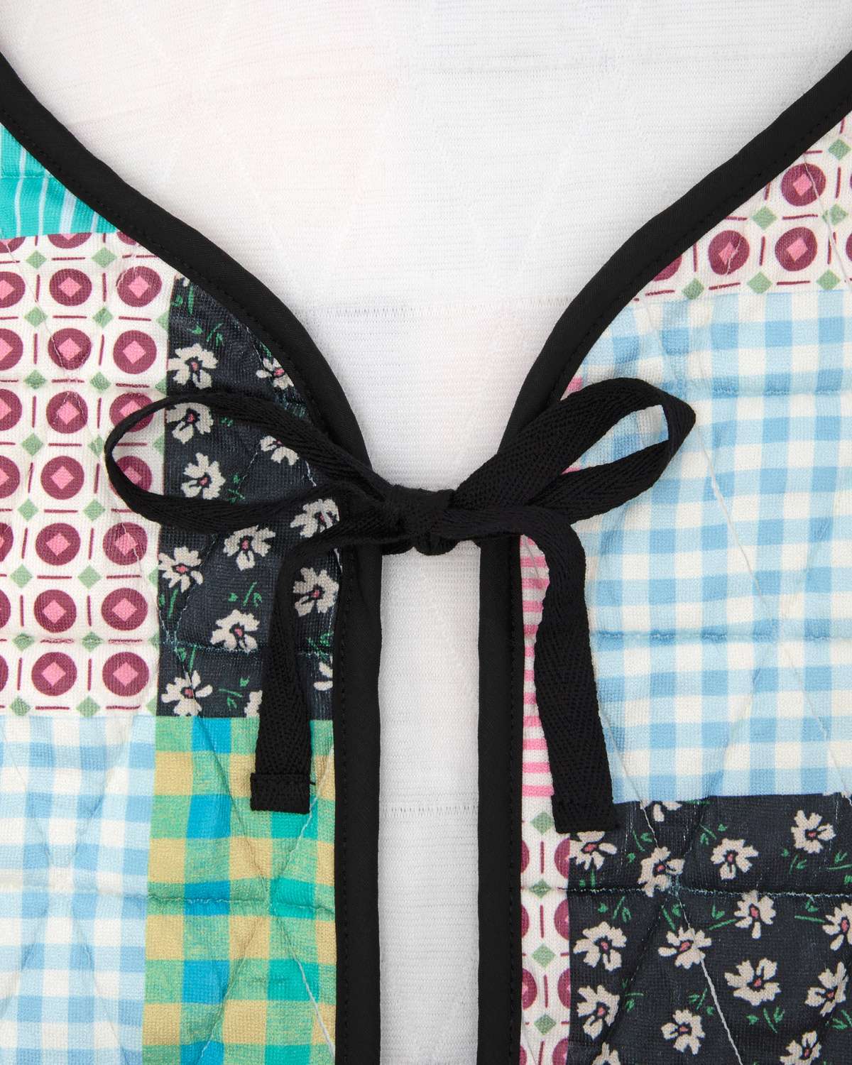 Up close of colorful patterned vest with a bow detail on a white background.