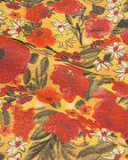 A close-up of a vintage floral fabric print featuring large red poppies, white daisies, and green leaves on a warm yellow background.