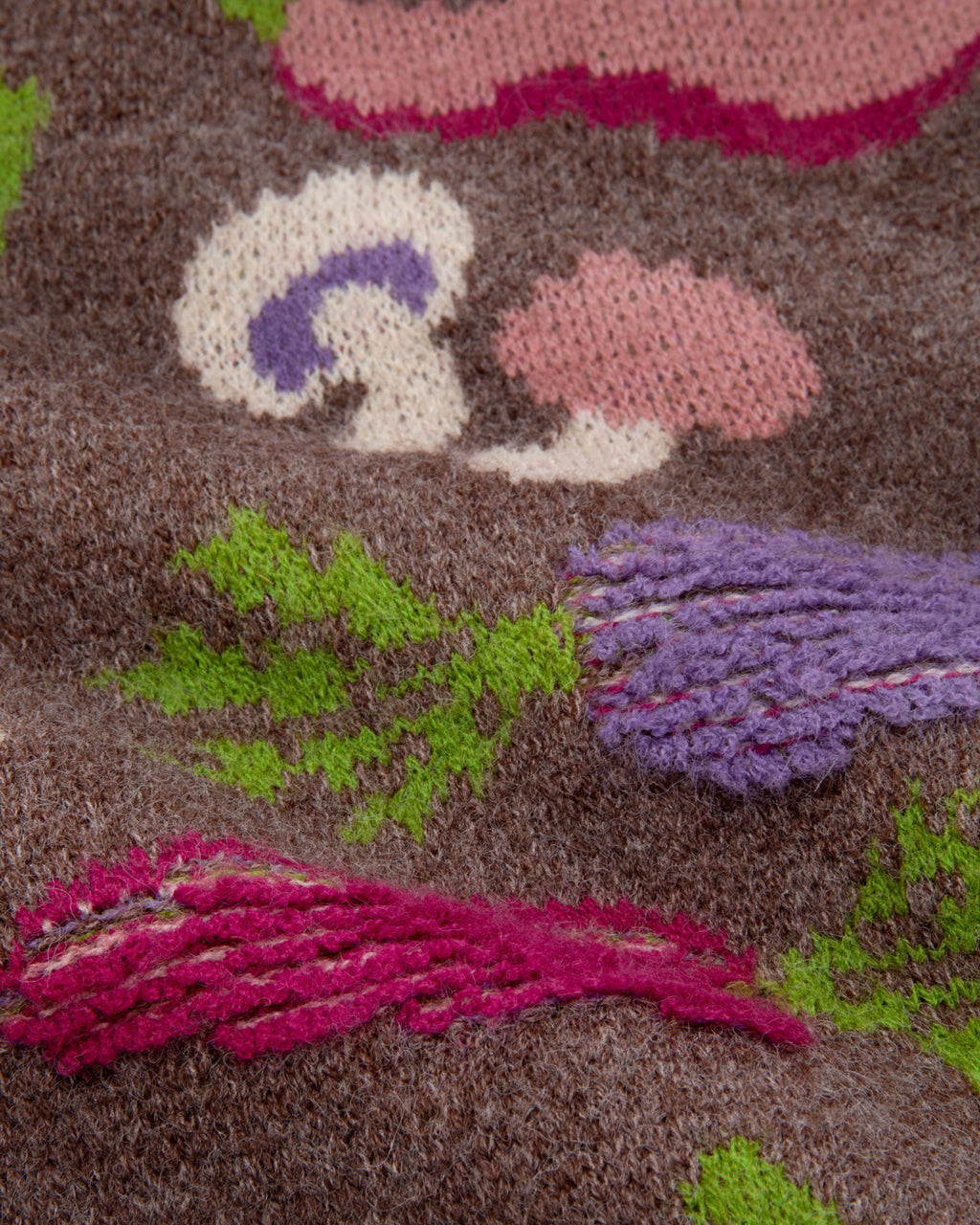 A close-up of a a chunky knit cardigan sweater with a multicolor vegetable pattern on a brown base. 