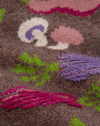 A close-up of a a chunky knit cardigan sweater with a multicolor vegetable pattern on a brown base. 