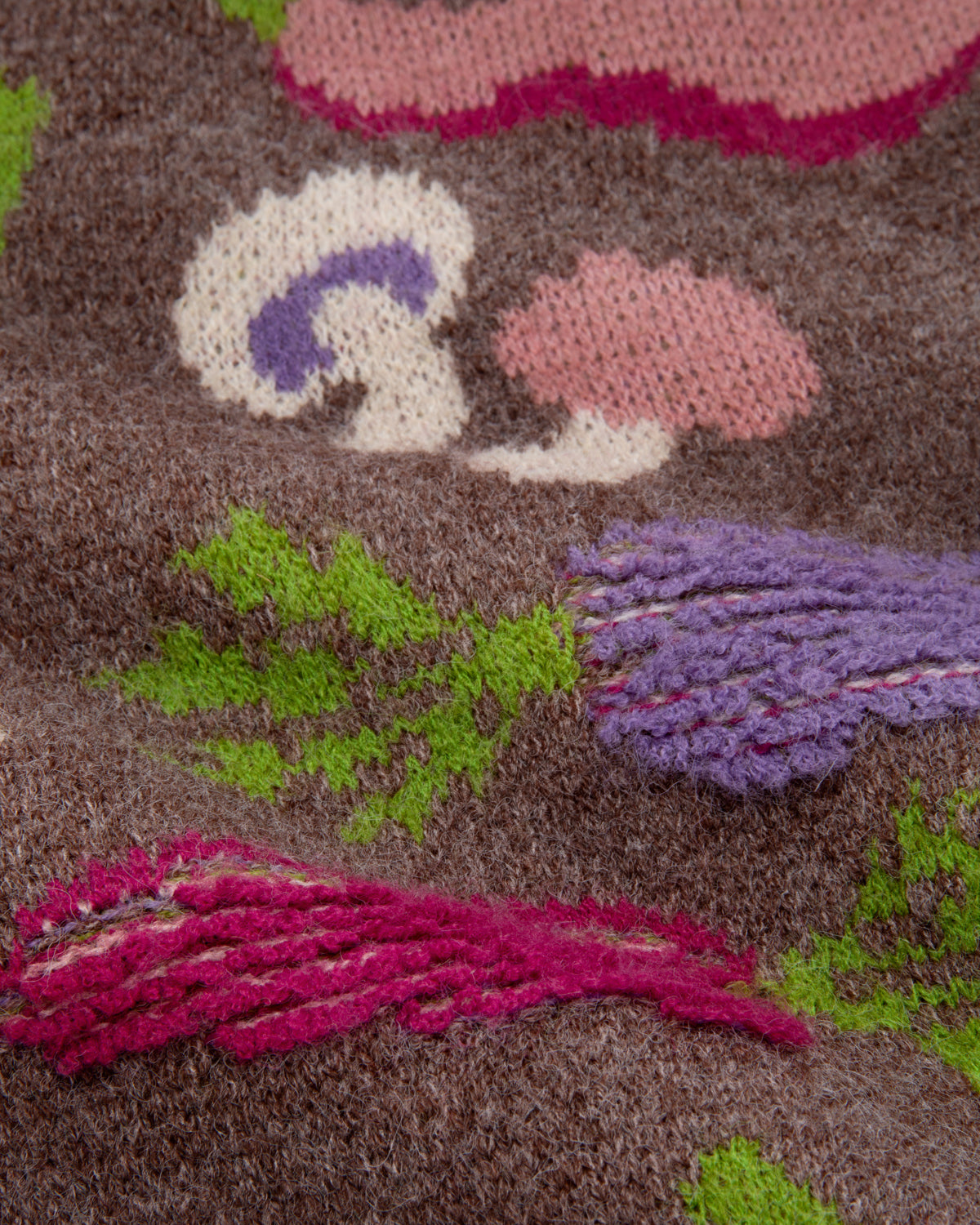 A close-up of a a chunky knit cardigan sweater with a multicolor vegetable pattern on a brown base. 