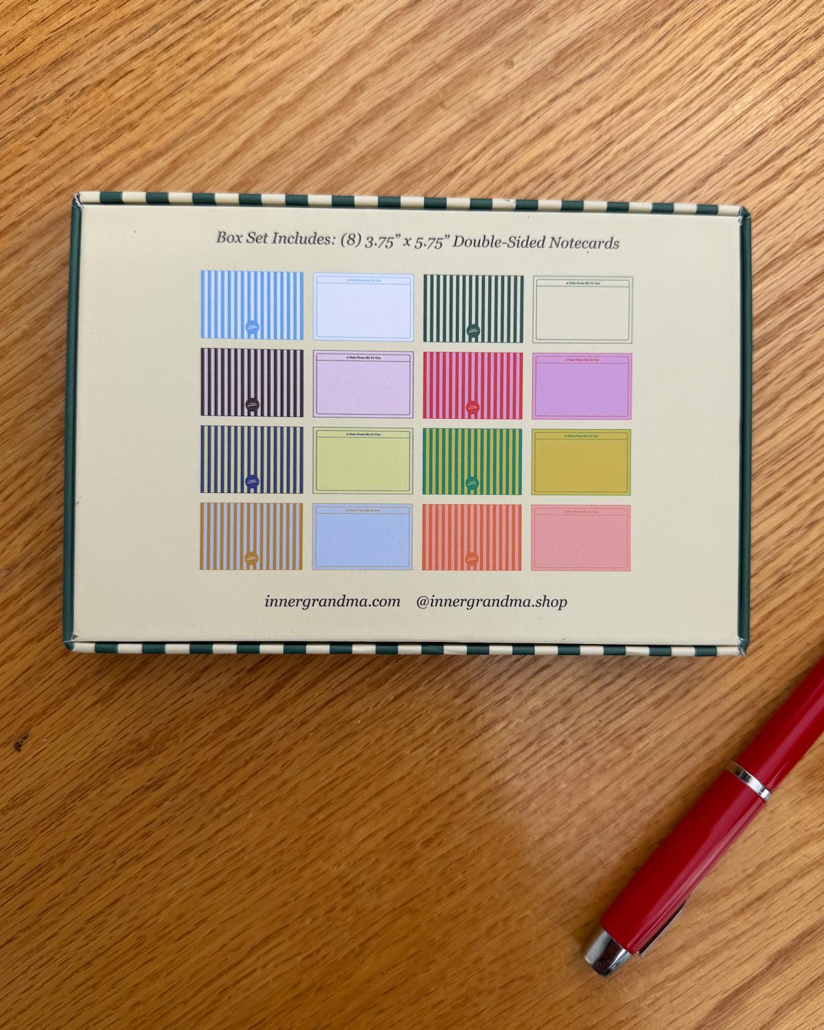Box of double-sided note cards with color swatches on a wooden surface, accompanied by a red pen.