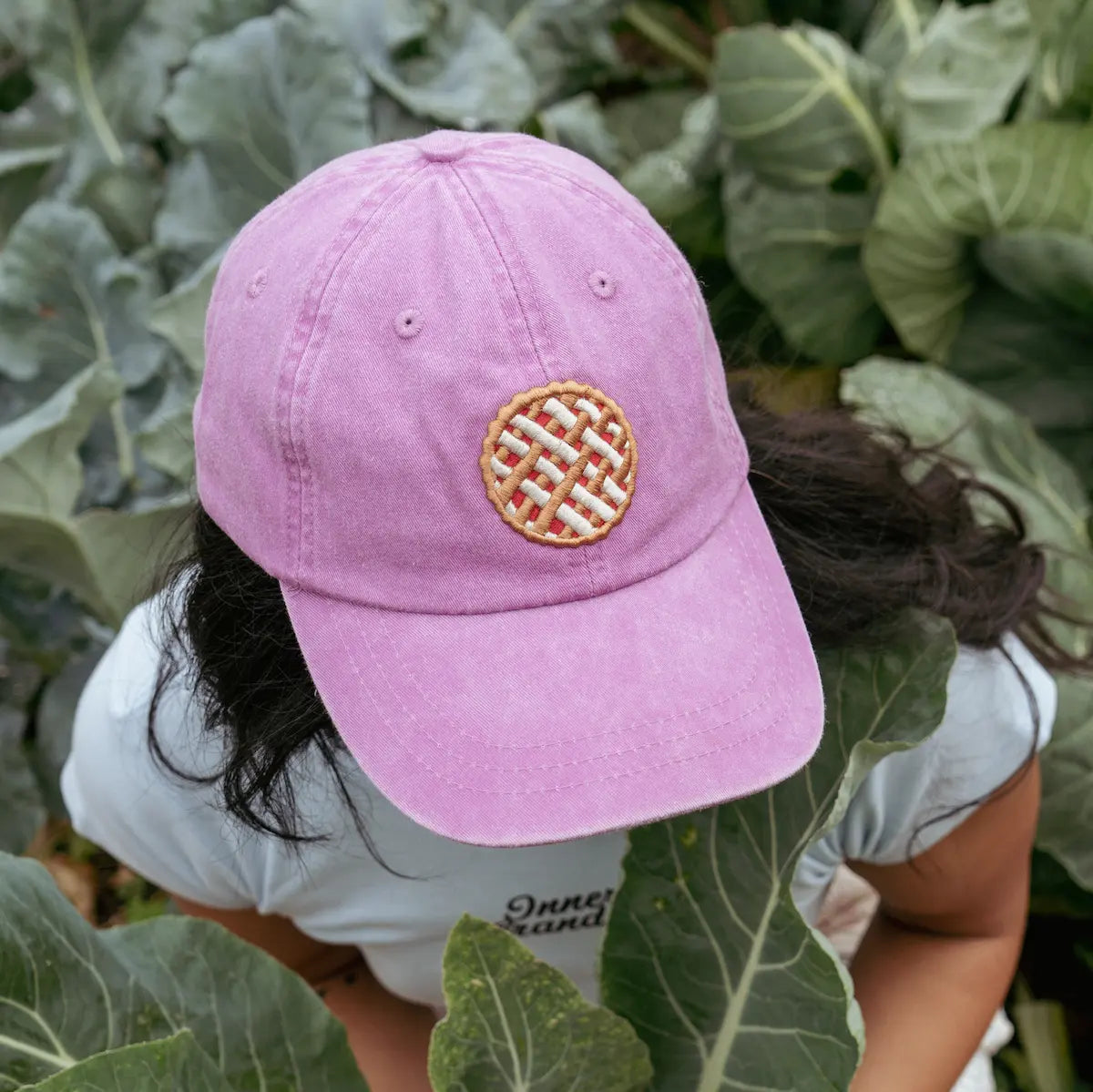 Person wearing a purple cap with a pie logo in a garden setting