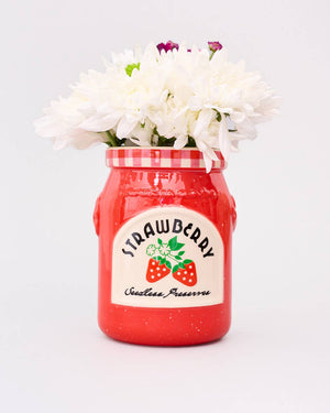 Red jar with strawberry preserve label filled with white flowers on a light gray background