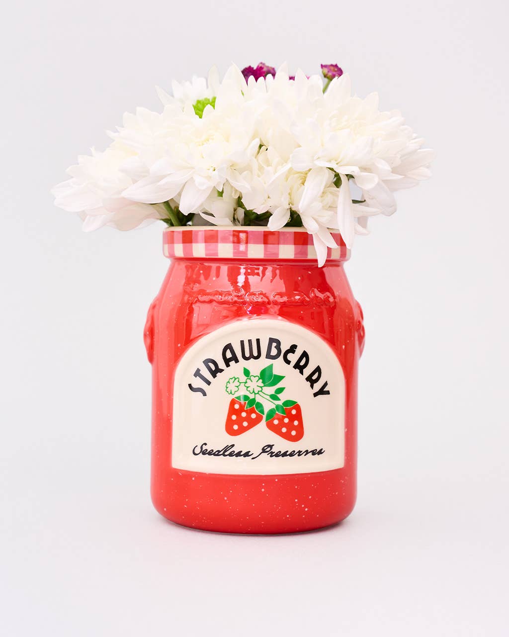 Red jar with strawberry preserve label filled with white flowers on a light gray background