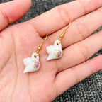 White teapot earrings with gold hooks on a hand