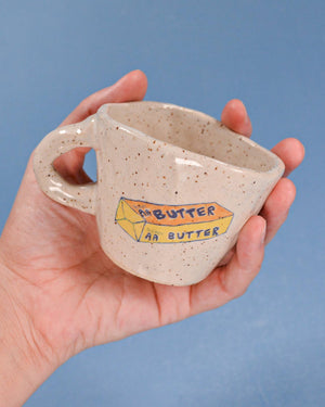 Hand holding a ceramic mug with 'Peanut Butter' label against a blue background
