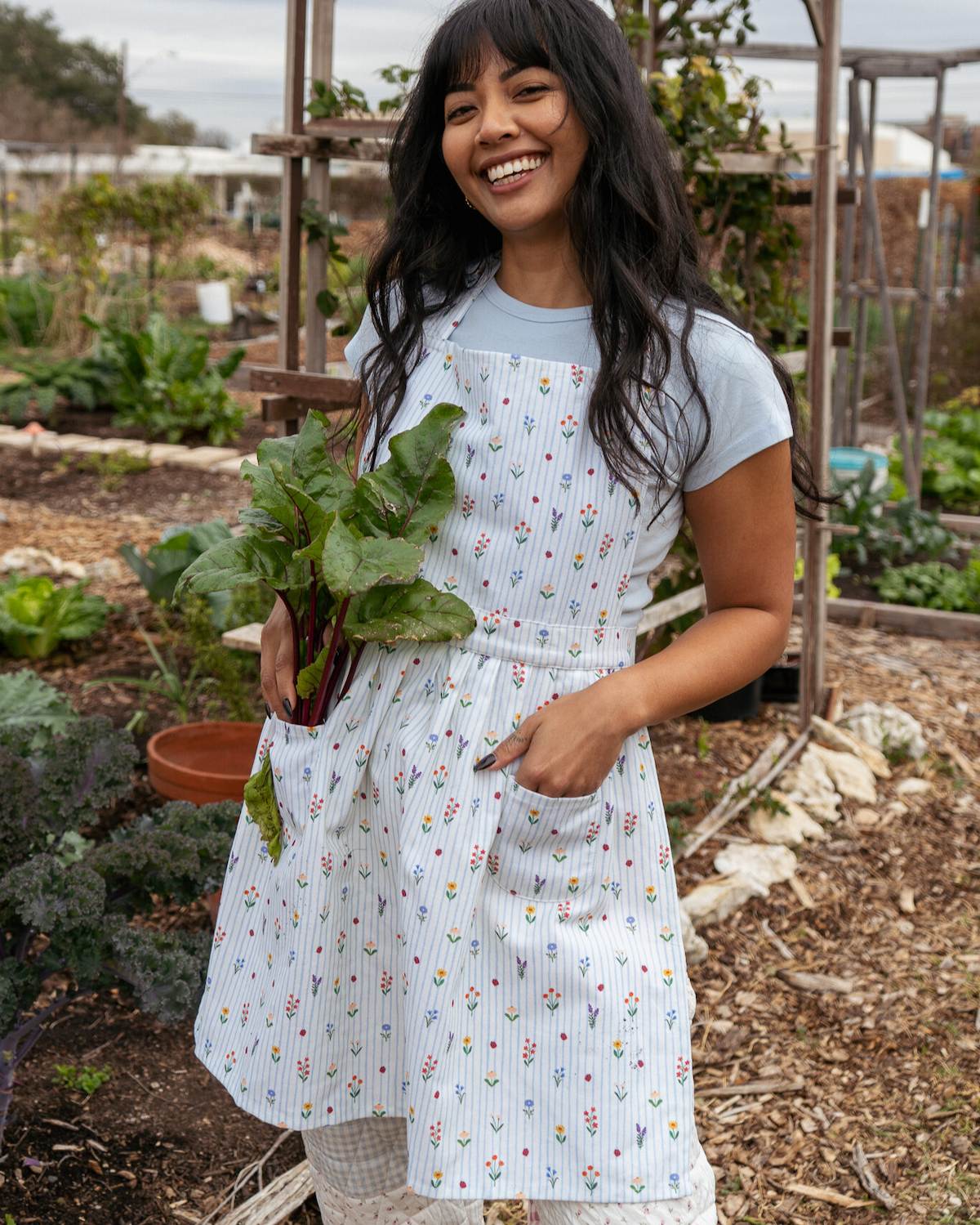 Woman in a garden holding fresh produce, wearing a patterned apron.