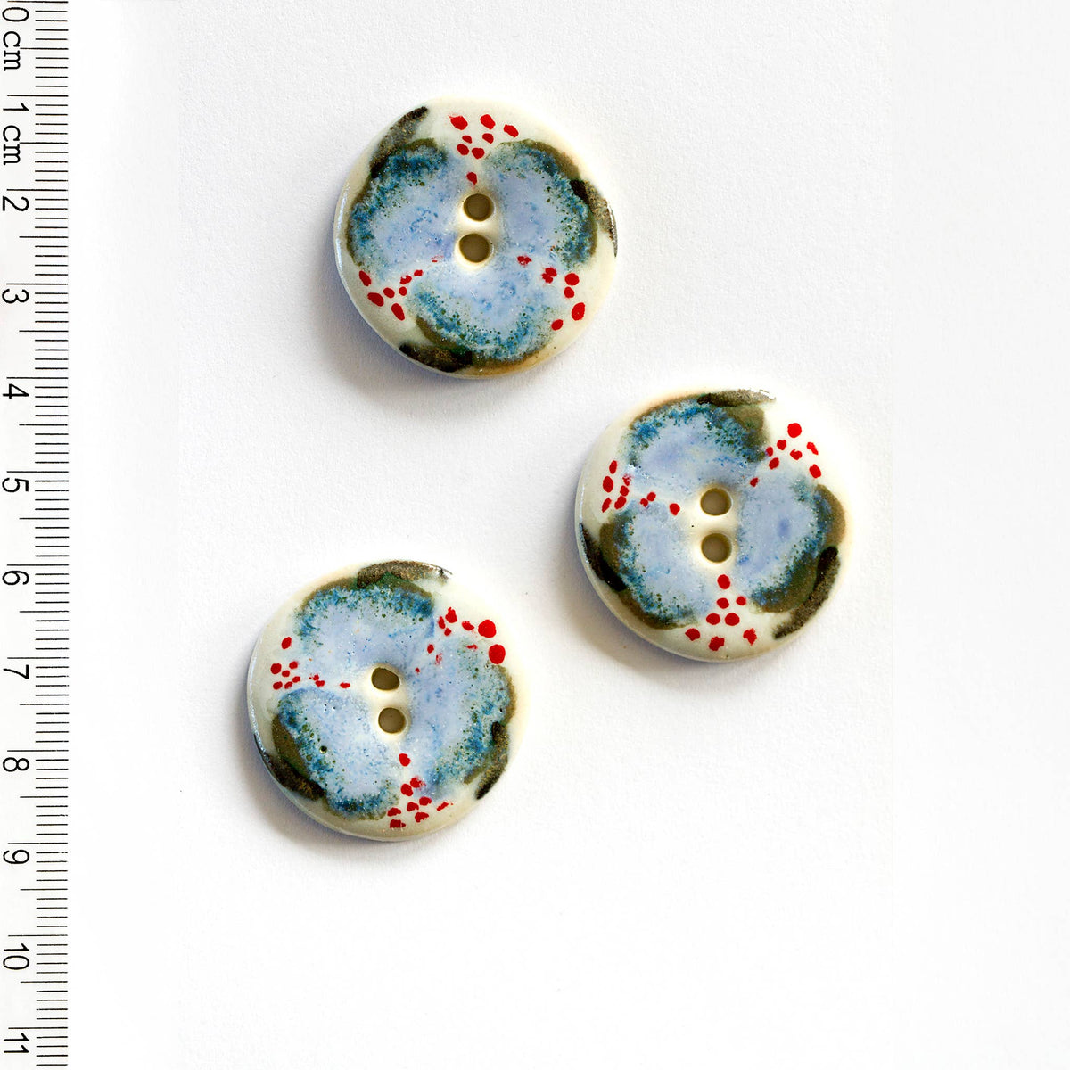 Three ceramic floral buttons with a blue and red pattern on a white background, accompanied by a ruler for scale.