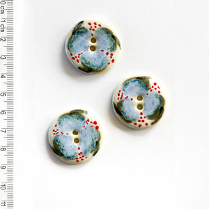Three ceramic floral buttons with a blue and red pattern on a white background, accompanied by a ruler for scale.