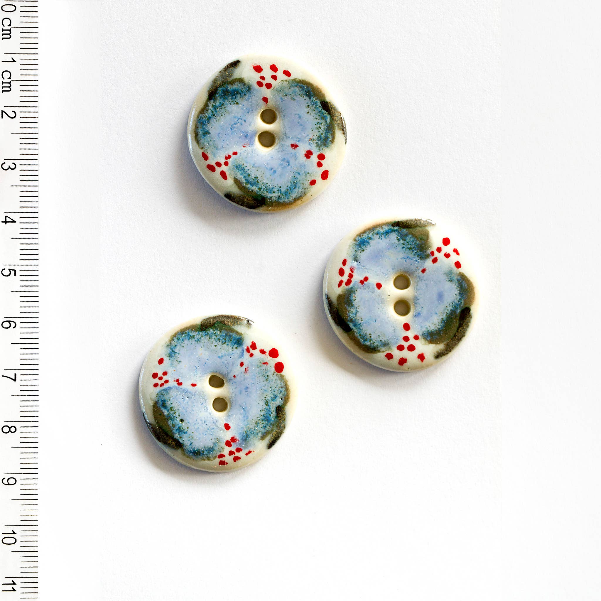 Three ceramic floral buttons with a blue and red pattern on a white background, accompanied by a ruler for scale.