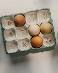 Eggs in a decorative carton with a measuring cup of flour on a light surface