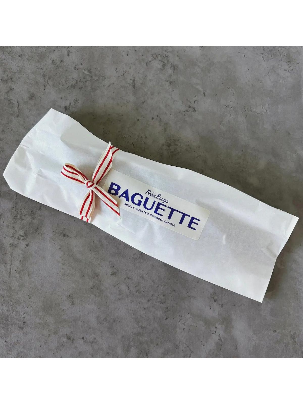 Baguette wrapped in white paper with a red and white ribbon on a gray surface