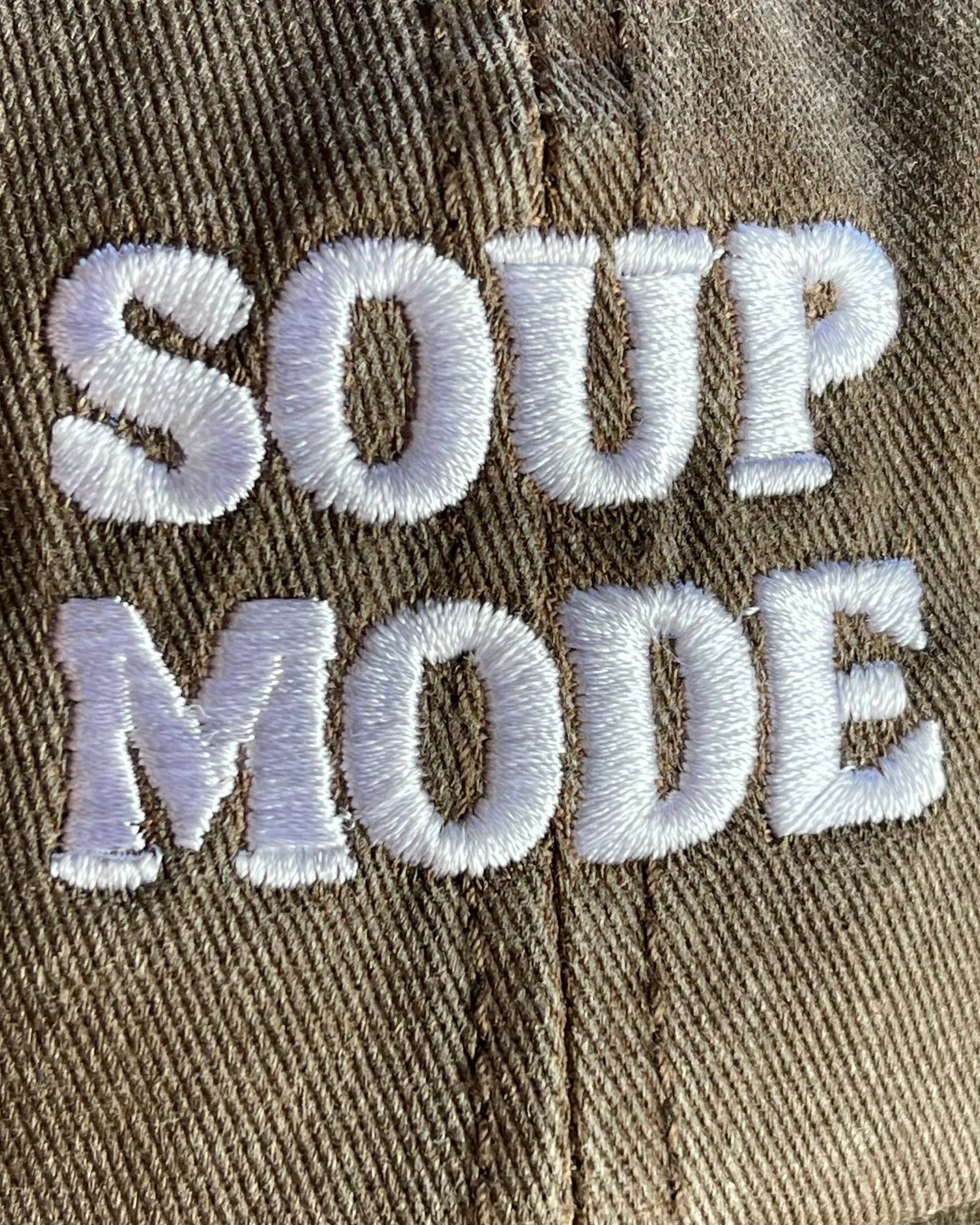 A close-up of a brown twill cap featuring white embroidered text that reads 'SOUP MODE'.