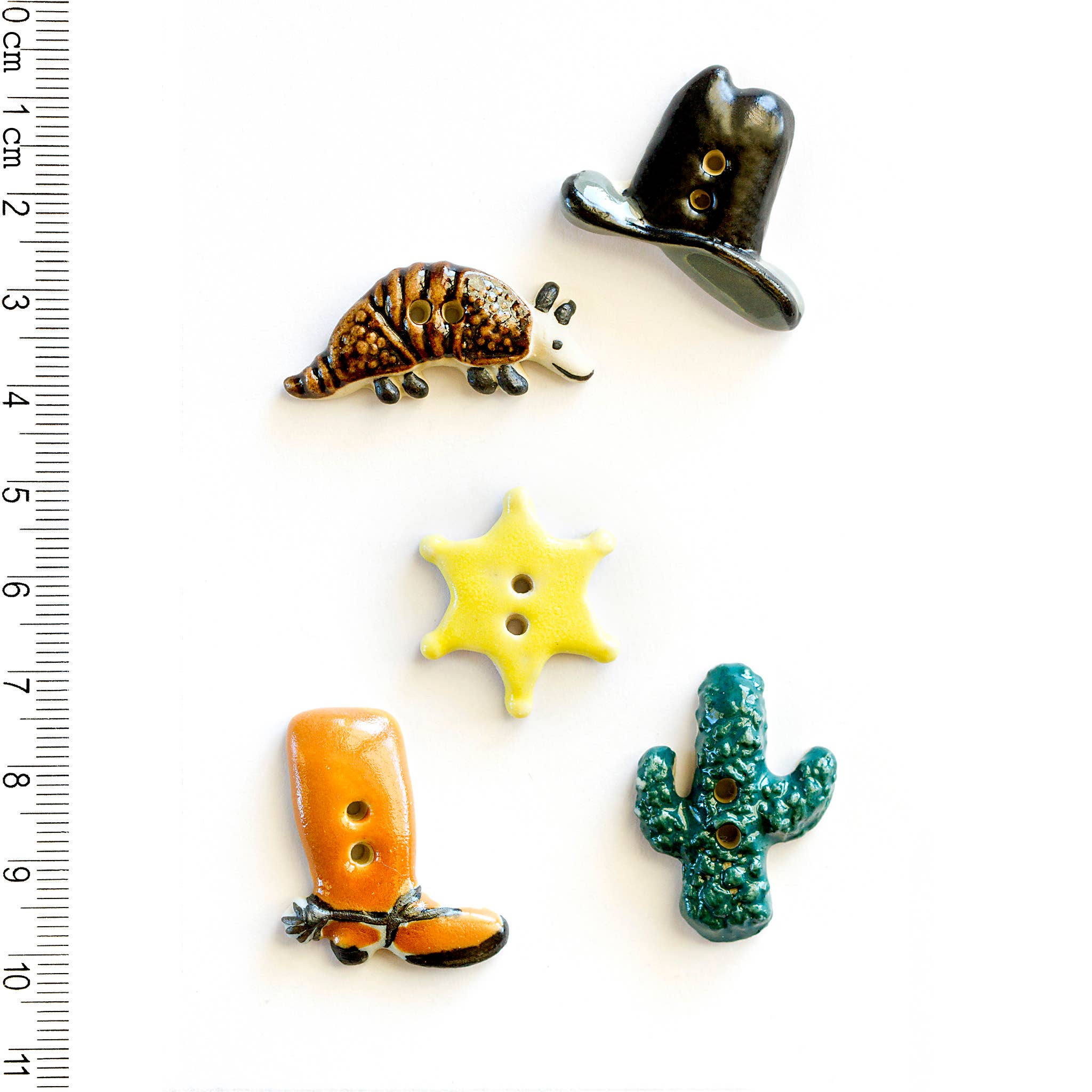 Set of decorative buttons including a boot, star, cactus, and cowboy hat on a white background with a ruler for scale.