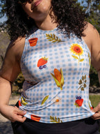 Person wearing a sleeveless top with colorful prints of vegetables and flowers on a checkered background.