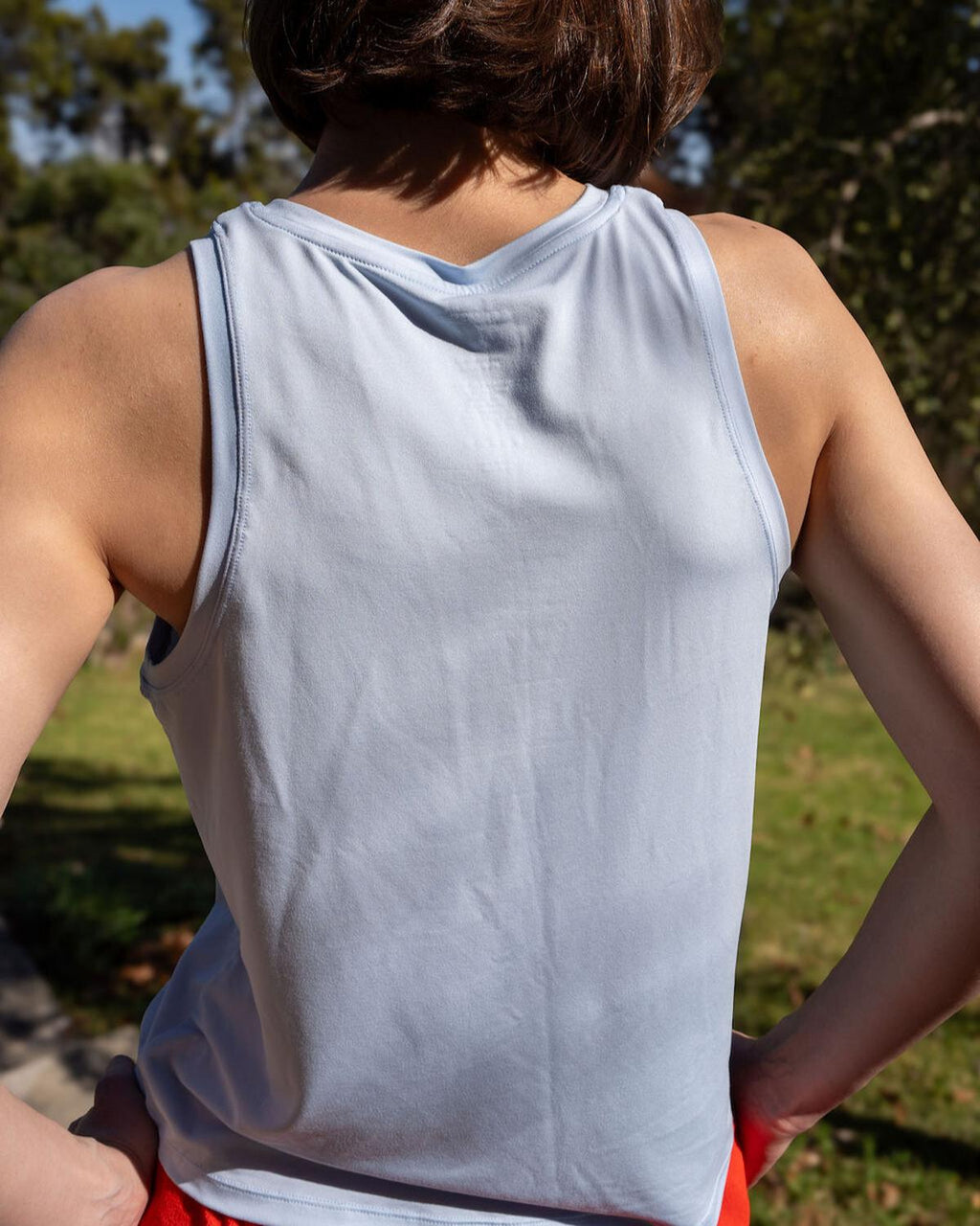 Person wearing a light gray tank top outdoors with greenery in the background